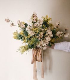 a bouquet of flowers is tied to the wall by someone's hand with a bow