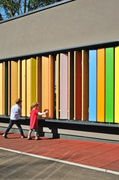 two people walking past a colorful wall on the side of a building