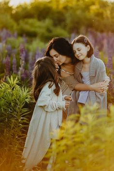 three girls hugging each other in the middle of a field of purple flowers at sunset