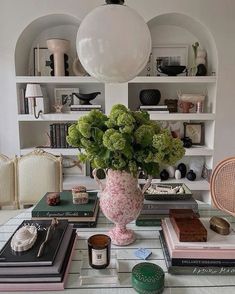 a table topped with books and a vase filled with green flowers next to two wicker chairs