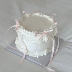 a white cake sitting on top of a plate with pink ribbon around it's edge