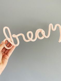 a hand holding up a string word that says dream in white letters on a gray background