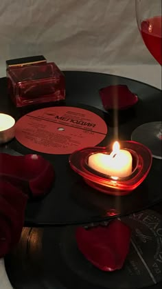 a table topped with candles and records next to a glass of red wine on top of it