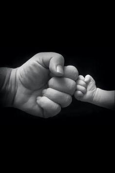 a black and white photo of a baby's hand holding the fist of an adult