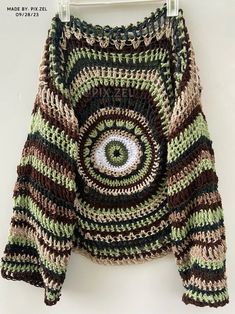 a crocheted sweater with an eye on the front and bottom, hanging from a hanger