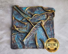 a blue and gold square sculpture with a medal on the left hand side that says genuine