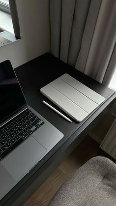 an open laptop computer sitting on top of a wooden desk next to a chair and window