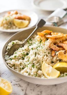 a bowl filled with rice and shrimp next to lemon wedges on a table top