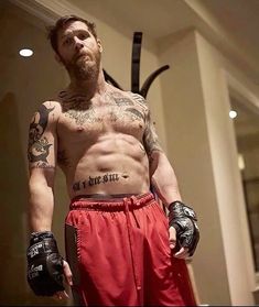 a man with tattoos on his chest wearing boxing gloves and holding a punching mitt