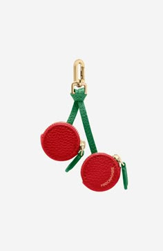 two red and green round objects hanging from a gold - plated hook on a white background