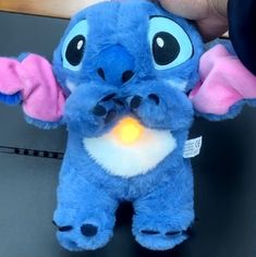 a blue stuffed animal with an orange light in it's mouth and ears, being held by someone