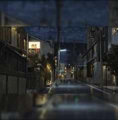 a city street at night with rain falling on the ground and buildings in the background