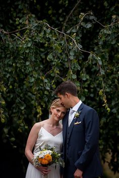 a bride and groom standing under a tree