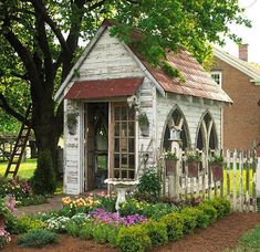 a garden shed with flowers and plants around it