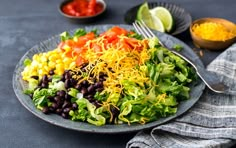 a salad with black beans, corn, tomatoes and cheese on a plate next to a fork