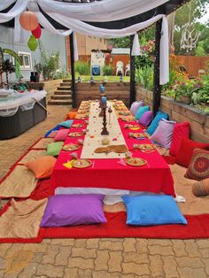 a long table is set up with colorful pillows and blankets on the ground for an outdoor party