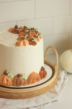 a white cake sitting on top of a wooden platter next to a small pumpkin