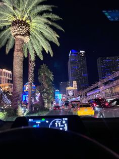 a car driving down a street at night with palm trees and buildings in the background