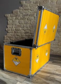 a yellow storage box sitting on top of a wooden floor next to a brick wall