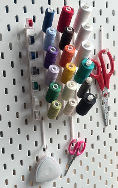 several spools of thread and scissors on a peg board