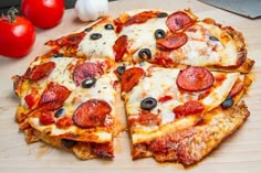 a pizza with pepperoni and olives on a wooden cutting board next to tomatoes