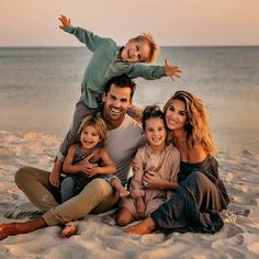 a family sitting on the beach with their arms in the air and smiling at the camera