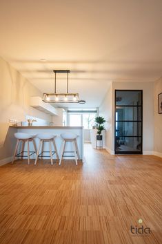 an empty kitchen and living room with hardwood floors, white counter tops and bar stools