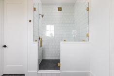 a bathroom with white tile and gold trim on the shower door, along with black flooring