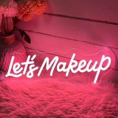 a pink neon sign that says let's make up on it next to a vase with flowers