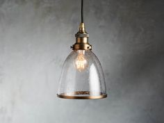 a glass and brass pendant light hanging from a ceiling fixture in an industrial style setting