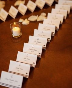 place cards are lined up on a table with a lit candle in the middle, along with seashells