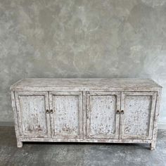 an old white wooden cabinet with three doors and two drawers on one side, against a gray wall