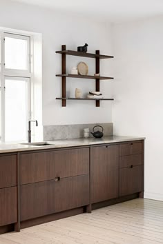 an empty kitchen with wooden cabinets and white walls, along with open shelves on the wall