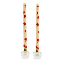 two candles with red flowers on them sitting side by side in front of each other