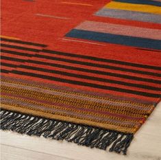 a multicolored area rug with fringes on the bottom and sides, laying on a wooden floor