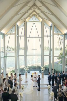 a bride and groom standing at the alter in front of their wedding party, surrounded by large windows