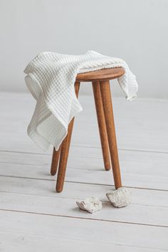 a wooden stool with a white blanket on it and two small rocks under the seat