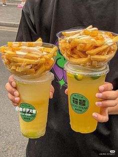 two people holding up cups filled with food on the side of the road in front of them