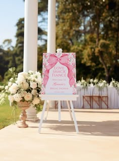 a sign that is on top of a stand with flowers in front of the sign