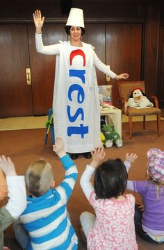 a woman dressed as pepsi standing in front of children sitting on the floor with their hands up