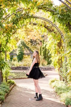 a woman in a black dress is standing under an arch