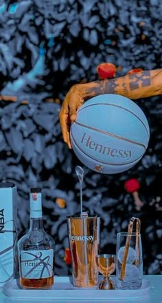 a person is holding a basketball above glasses and liquor bottles on a table with an advertisement in the background