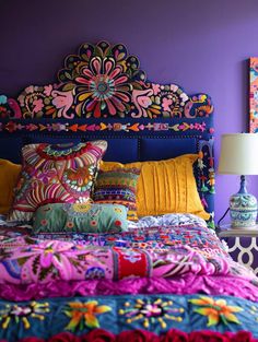 a bed with colorful pillows and blankets on it in a room that has purple walls