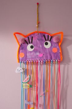 a purple cat made out of paper and streamers hanging from the wall with other items attached to it