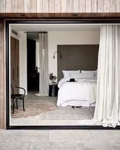 a bedroom with a large bed and white curtains on the window sill in front of it