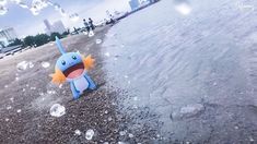 a pokemon stuffed animal sitting on top of a sandy beach next to the ocean with bubbles floating over it