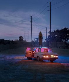 a woman standing on top of a car in the middle of a field at night