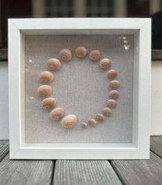 a white frame with shells arranged in the shape of a circle on top of a wooden table