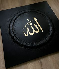 an arabic calligraphy is displayed on a black surface with gold lettering and wood flooring