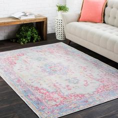 a white couch sitting next to a rug on top of a hard wood floor covered in pink and blue colors